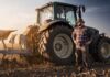Farmer standing beside a tractor in a plowed field