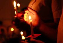 Hands holding lit candles in a dark setting