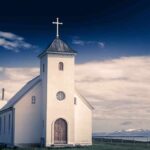 White countryside church with steeple and cross under a dramatic sky
