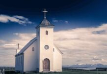 White countryside church with steeple and cross under a dramatic sky