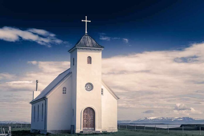shutterstock_1041609115 White countryside church with steeple and cross under a dramatic sky