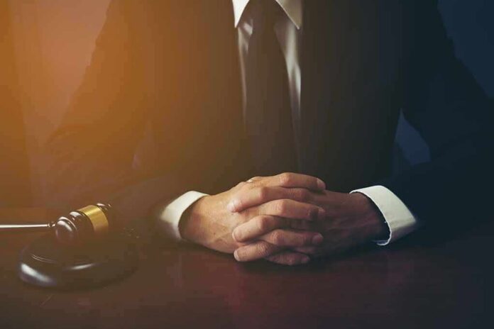 shutterstock_1049502869 person in suit with hands clasped at a desk beside a gavel