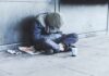 Person sitting on a sidewalk with head down and hood up