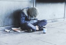 Person sitting on a sidewalk with head down and hood up