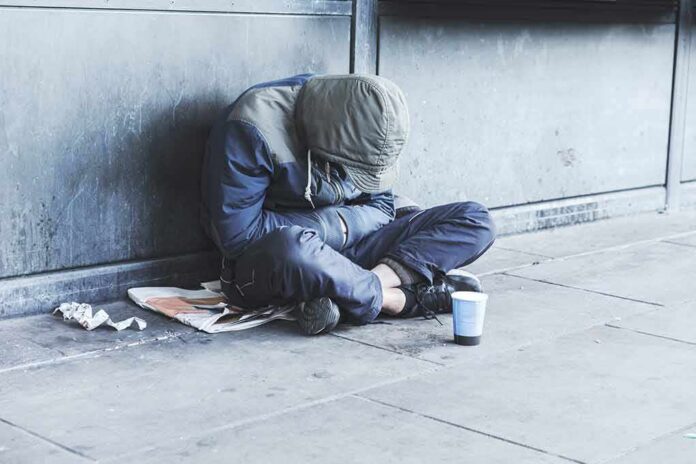 Person sitting on a sidewalk with head down and hood up