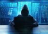 Hooded figure using a laptop in front of glowing code