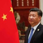 Red-Carpet Trap For Xi? Tarmac Power Move Ups The Stakes Xi Jinping standing beside a Chinese flag