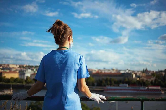 shutterstock_1807283785 Healthcare worker in blue scrubs overlooking a cityscape