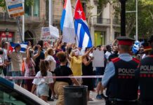 Sanctions Squeeze Cuba – Pentagon Waits Quietly Walter Jones amid crowd at street protest with Cuban flags and police present