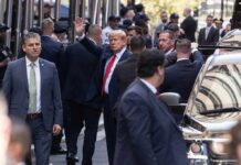 Donald Trump waving while surrounded by security personnel on a city street
