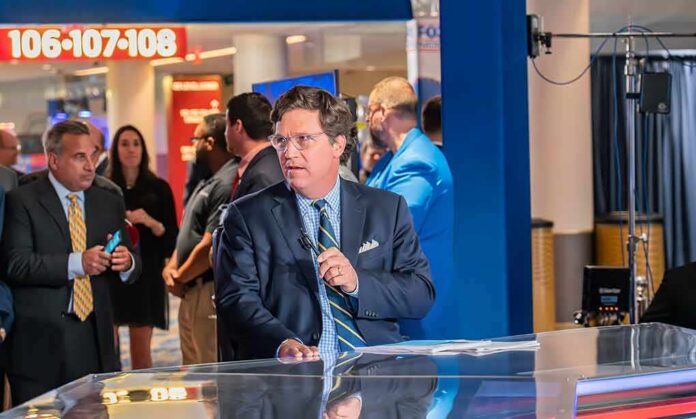 shutterstock_2329709309 Tucker Carlson at a news desk in a busy studio setting