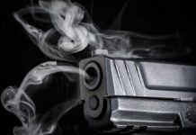Close-up of a handgun muzzle with smoke swirling from the barrel