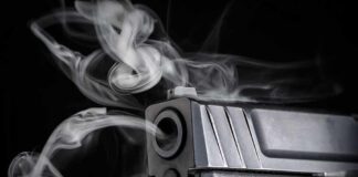 Close-up of a handgun muzzle with smoke swirling from the barrel