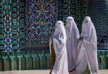Three women in white veils walking past ornate blue tilework