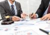 Oldest Winery Buckles Under Massive Debt Two businesspeople in suits reviewing charts at a desk with a gavel