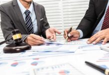 Two businesspeople in suits reviewing charts at a desk with a gavel