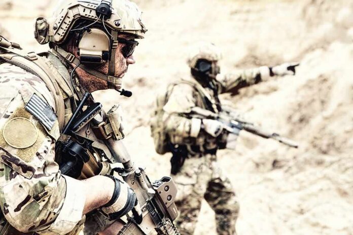 Soldiers in camouflage gear with rifles in a sandy terrain