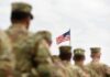 Iran War Tab: What’s Not Counted? U.S. flag flying above a formation of soldiers in uniform