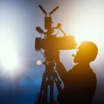 Silhouette of a camera operator adjusting a video camera on a tripod