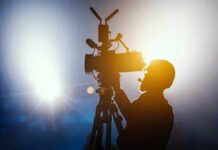 Silhouette of a camera operator adjusting a video camera on a tripod