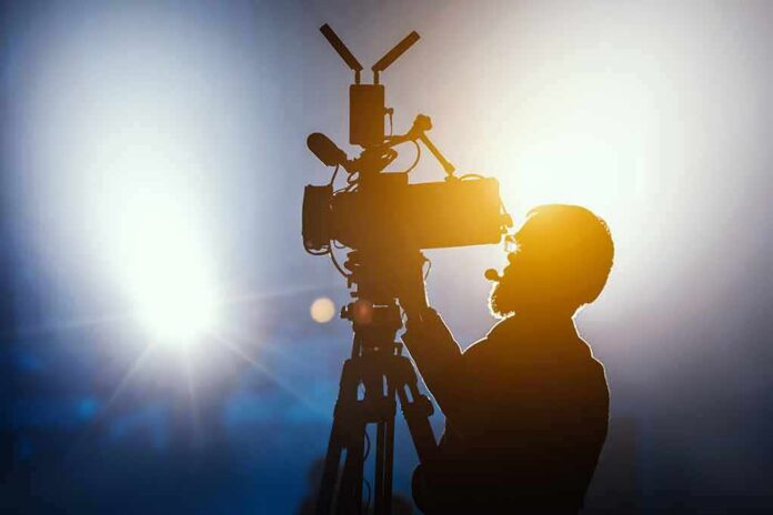 shutterstock_1297145938 Silhouette of a camera operator adjusting a video camera on a tripod