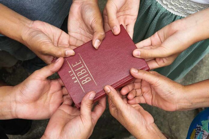Multiple hands holding a red Bible