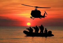 Cold, Pain, Laughter – SEAL Survival Code Helicopter hovers above armed team in inflatable boat at sunset