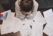 Person with head in hands surrounded by scattered papers and credit cards