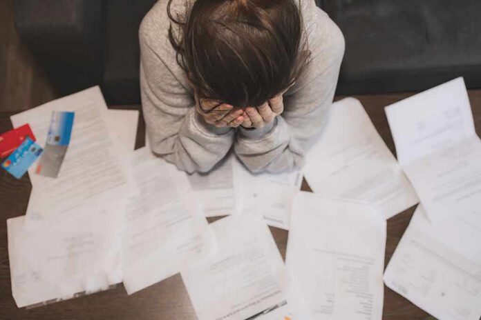 shutterstock_1639896217 Person with head in hands surrounded by scattered papers and credit cards