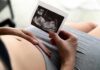 Taxpayer Tab for IVF? Grindr’s Gamble Pregnant person holding an ultrasound photo over their belly