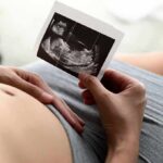 Taxpayer Tab for IVF? Grindr’s Gamble Pregnant person holding an ultrasound photo over their belly