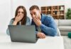 Two people cover their mouths while looking at a laptop