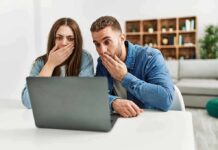Two people cover their mouths while looking at a laptop