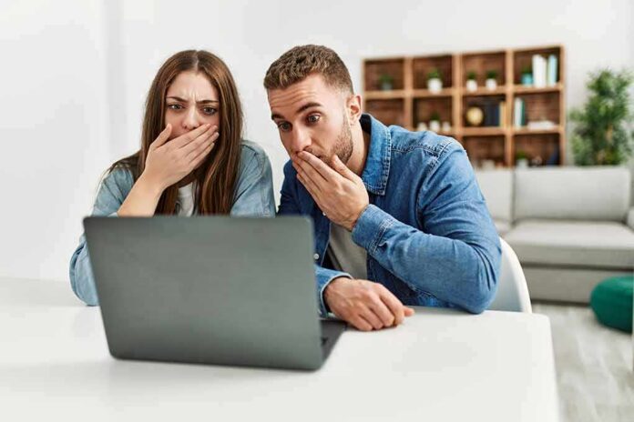 Two people cover their mouths while looking at a laptop