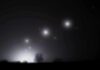 Night sky over a silhouetted landscape with glowing orbs of light
