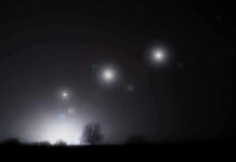 Night sky over a silhouetted landscape with glowing orbs of light