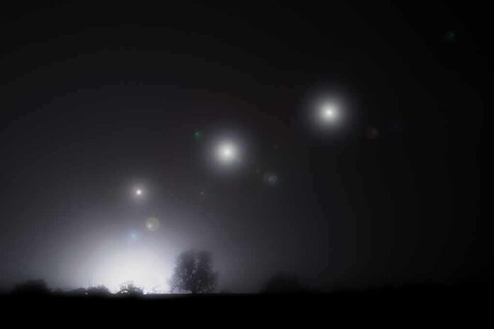 shutterstock_2239085913 Night sky over a silhouetted landscape with glowing orbs of light