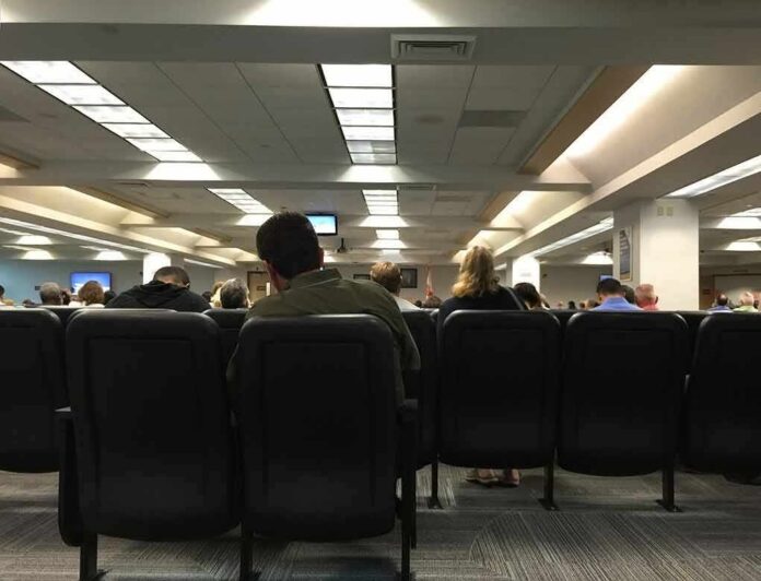 shutterstock_559969699-1 People seated in a waiting room with rows of chairs