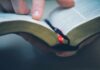 Hand holding an open book with a finger pointing at text