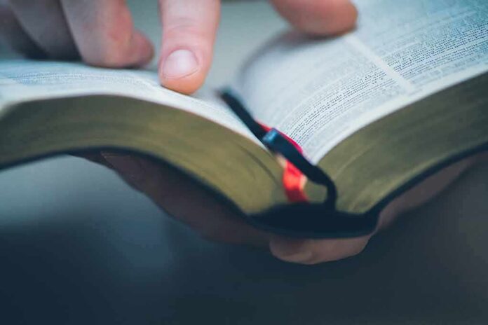 shutterstock_588422027 Hand holding an open book with a finger pointing at text