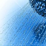 Close-up of a shower head with water droplets against a blue background